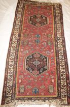 An old Eastern hand-knotted wool rug with geometric decoration on red and brown ground,