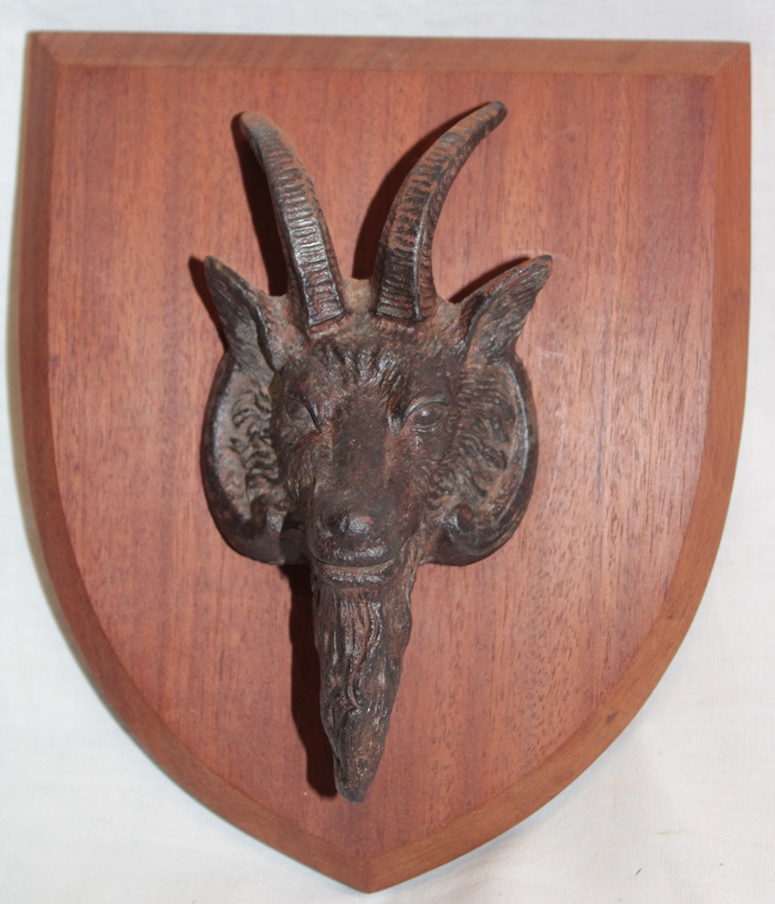 An old cast-iron plaque of a billy goat's head, mounted on a wooden shield,