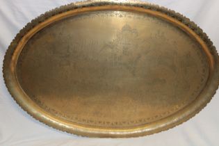 A large Middle Eastern brass oval tray engraved all over with numerous figures,