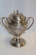 A George III silver circular two-handled pedestal cup and cover decorated in relief with two