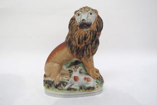 A 19th Century Staffordshire seated lion with lamp sat between its feet, 17cm tall x 12.5cm tall