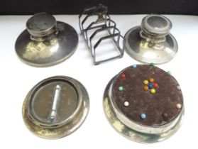 Two silver capstan inkwells, a pincushion, desk thermometer and a five bar toast rack (5)