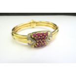 A gold sprung bangle with a cabochon ruby studded centre flanked by diamonds, stamped 750, 38.6g
