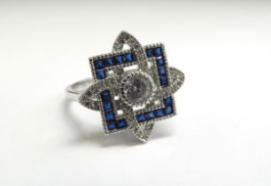 A dress ring with centre white stone in halo of blue stones with white stone set swirls, stamped
