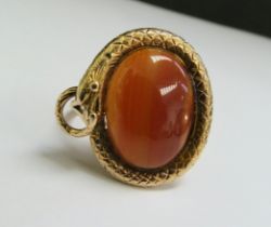 A gold ring with an oval cabochon cornelian in a snake surround, stamped 9ct. Size Q/R, 8.3g