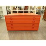 An orange painted four drawer Plan chest in Beech ply, with inset handles and set of four castors.