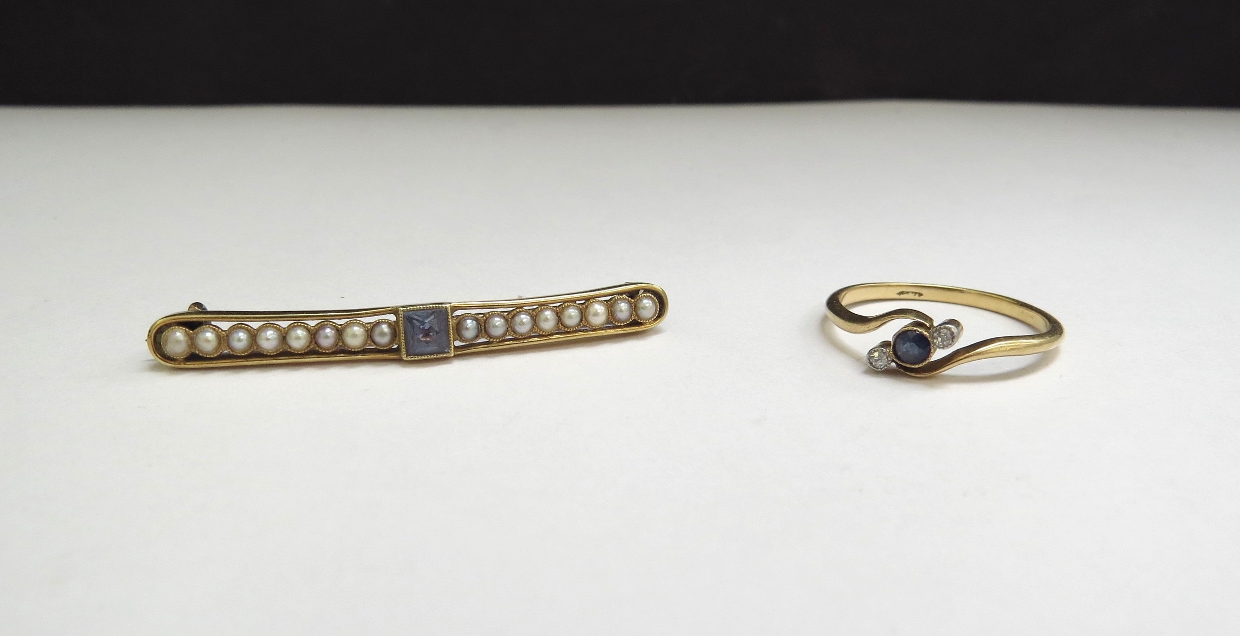 A gold bar brooch centrally set with a square sapphire flanked by a row of seed pearls, stamped