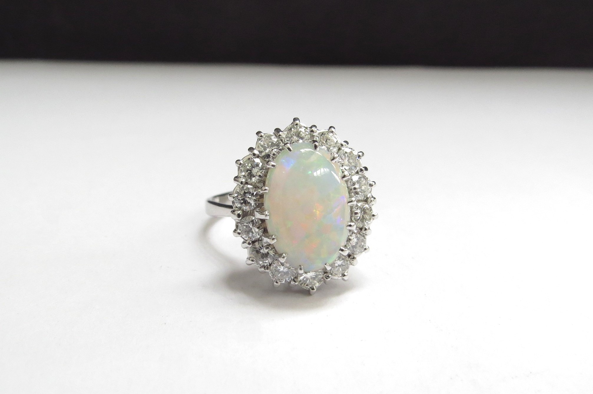 An 18ct white gold opal and diamond cluster ring the centre oval opal 14mm x 9mm framed by 14