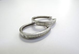 A pair of white gold elongated hoop earrings, the front half with a line of baguette diamonds,