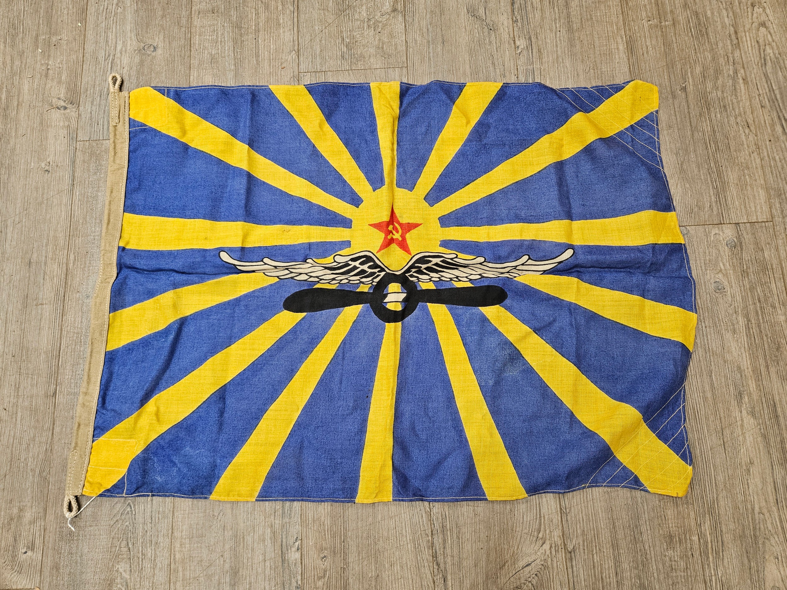 A Russian USSR Soviet Air Force flag, yellow sun rays on a blue ground with wings and propeller