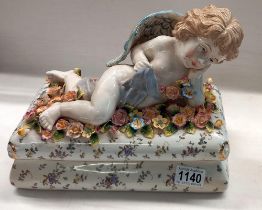 A large continental glazed bisque lidded box of a reclining cherub