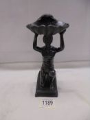 A bronze figure of a kneeling man holding a large shell above his head.