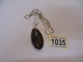 A large oval amber pendant in silver mount and on silver chain.