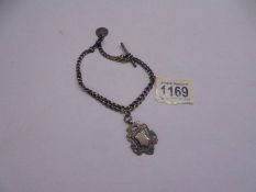 A metal watch chain with a silver fob and a silver coin attached.