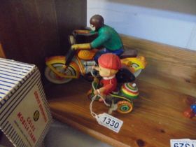 A vintage clockwork motorcycle and a boy on a tricycle.
