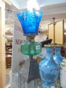 An oil lamp on a cast iron base with a green glass font and a later blue glass shade, COLLECT ONLY.