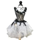 A mannequin with black netting bodice and white netting skirt with decorative embellishments