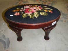 An oval footstool with cross stitch top.