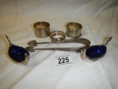 Three silver napkin rings, two plated salts with blue glass linings and a pair of sugar nips.