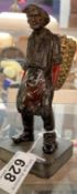 A Cast metal peasant figure carrying a large basket in traditional dress on slate base. Height 17cm
