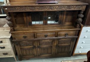 An Oak buffet with carved and decorated detail and turned baluster supports glazed centre doors to