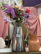 A tall metal jug with artificial flowers & a terracotta jug