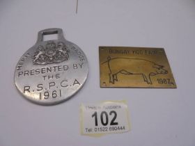 A 1961 RSPCA merit badge and a Bungay Hog Fair 1987 brass plaque.