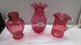 Three cranberry glass jugs.