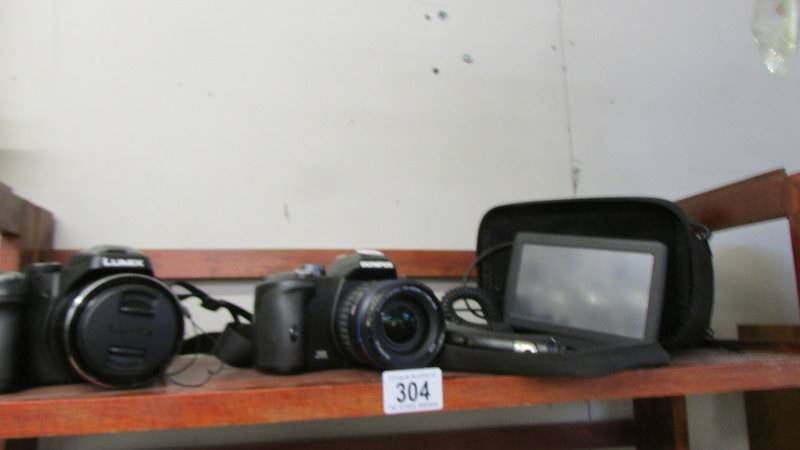 A Lumix camera, an Olympus camera, a camera case and a sat nav.