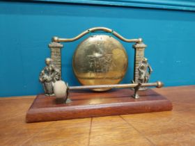 1950's brass gong on wooden base surmounted by Lady and Gentleman. {17 cm H x 28 cm W x 10 cm D}.