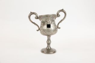 A pewter 2 handled prize footed cup, embossed with flowers and scrolls, a panel on one side engraved