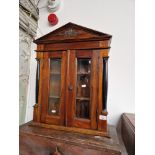 A glazed mahogany wall cabinet with bevelled glass and flanked by ebonised columns.