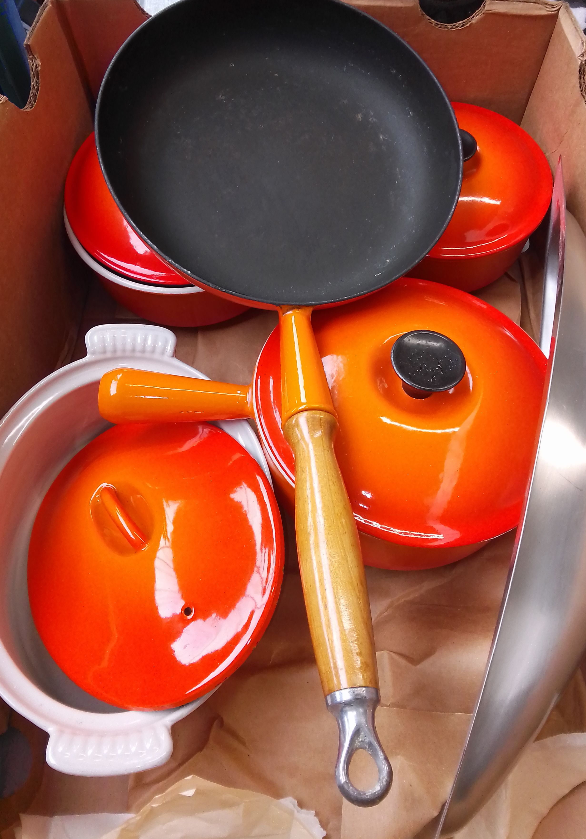 A ox containing 3 Le Creuset sauce pans and a Le Creuset style frying pan and casserole dish