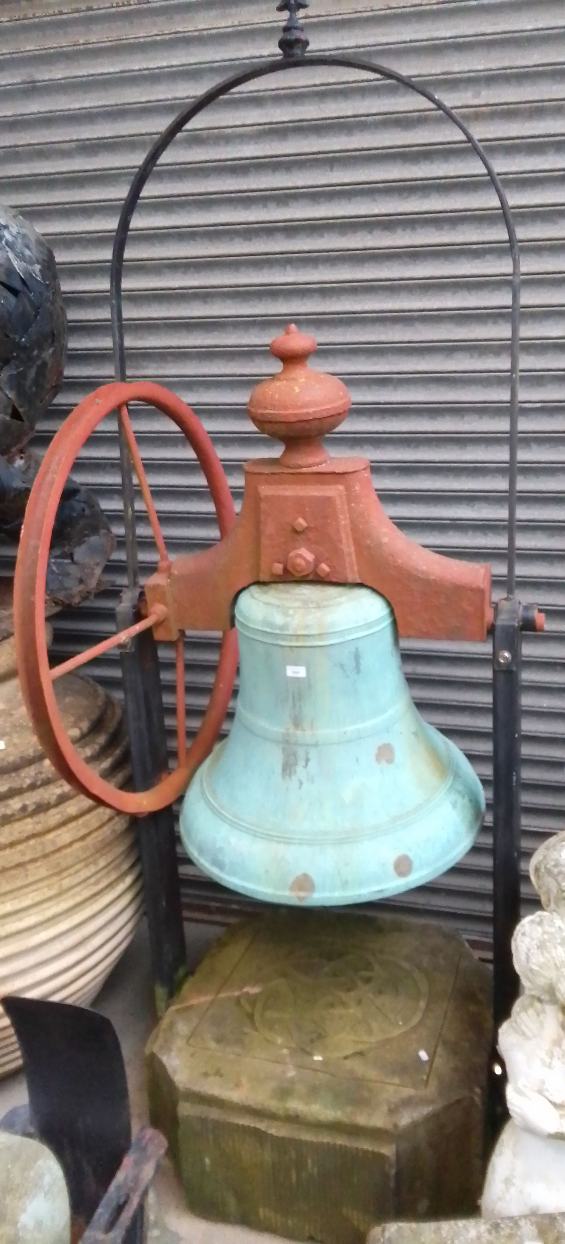 A very large bronze bell on a metal frame with a large stone base and metal wheel