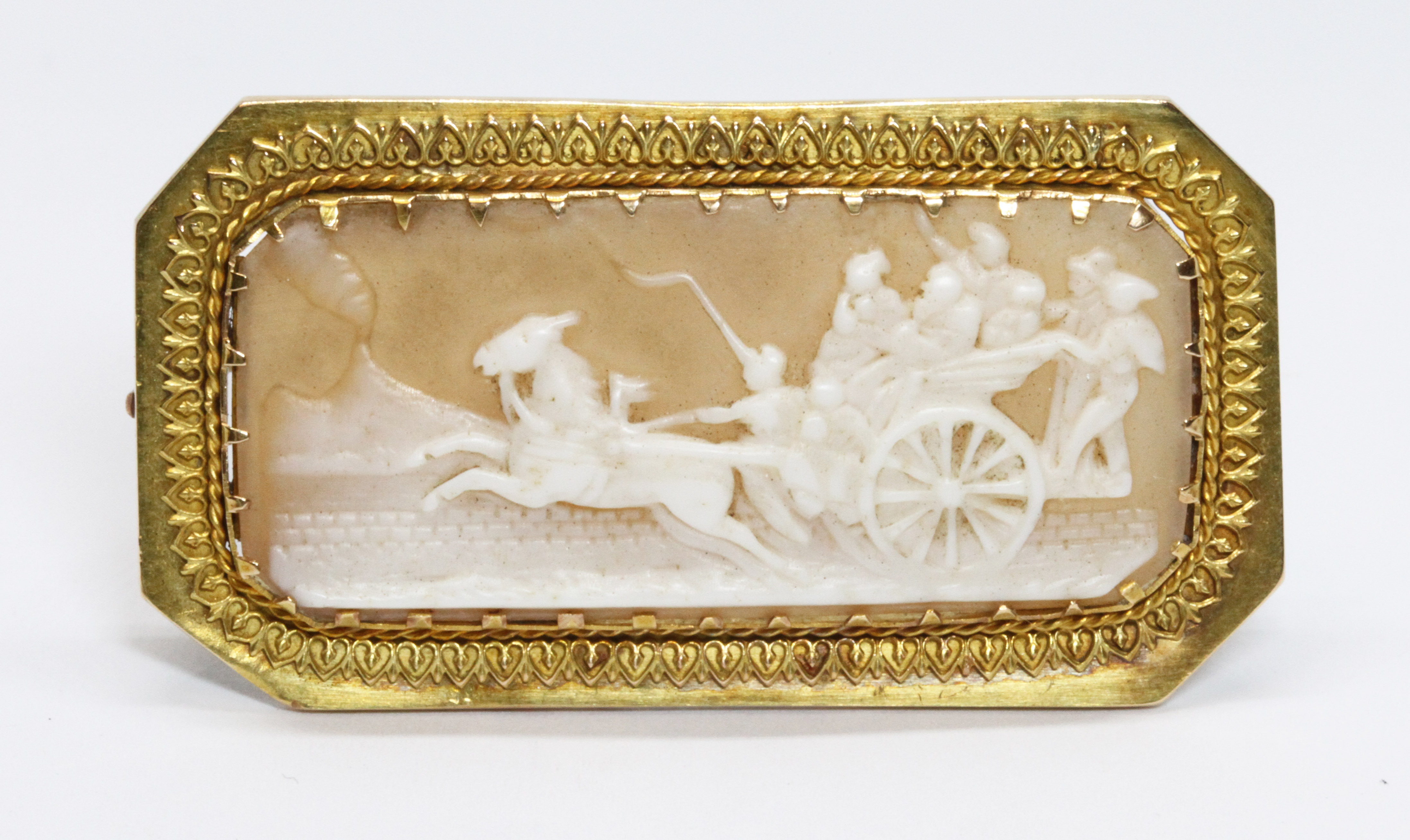 A yellow metal cameo brooch, the rectangular shell cameo depicting figures riding a chariot with