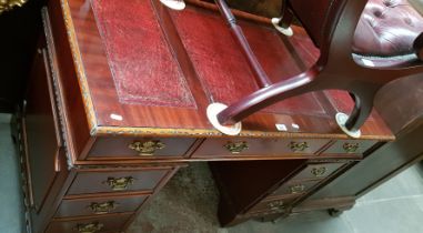 A mahogany pedestal desk with tooled red leather writing surface.
