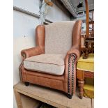 A modern wingback armchair with tan leather style upholstery.