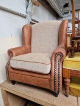 A modern wingback armchair with tan leather style upholstery.