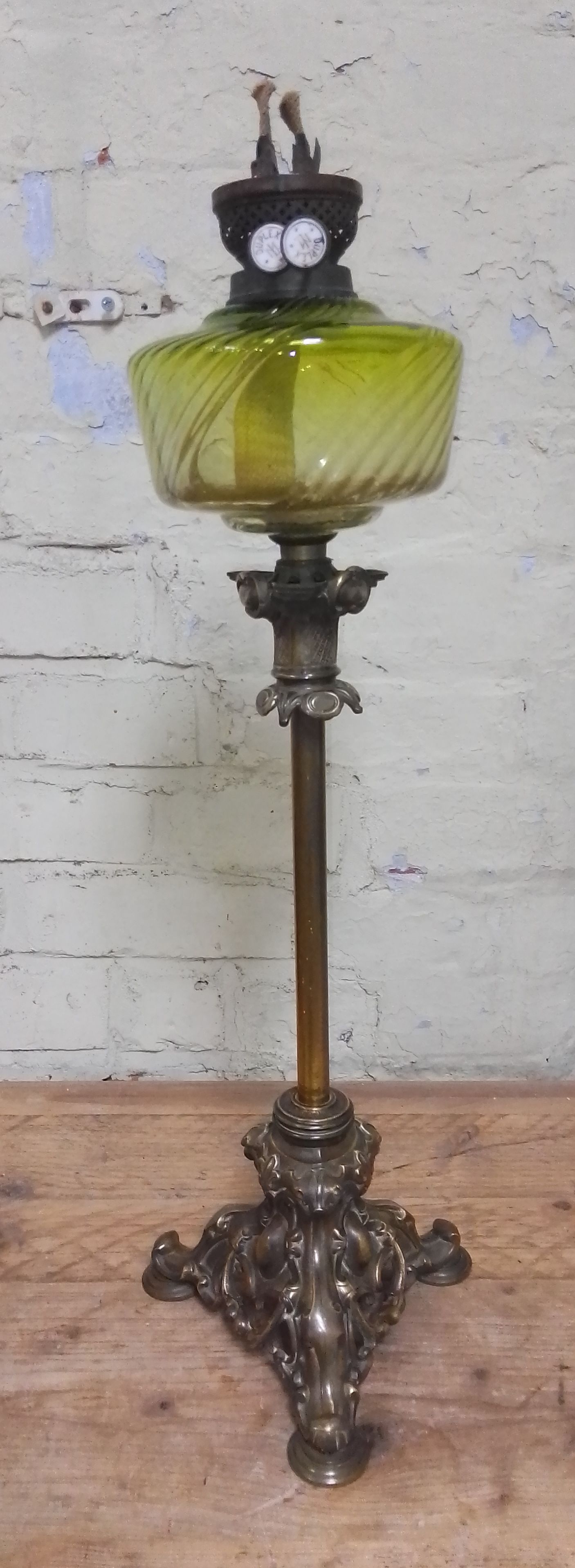 A cast brass oil lamp with green glass reservoir.