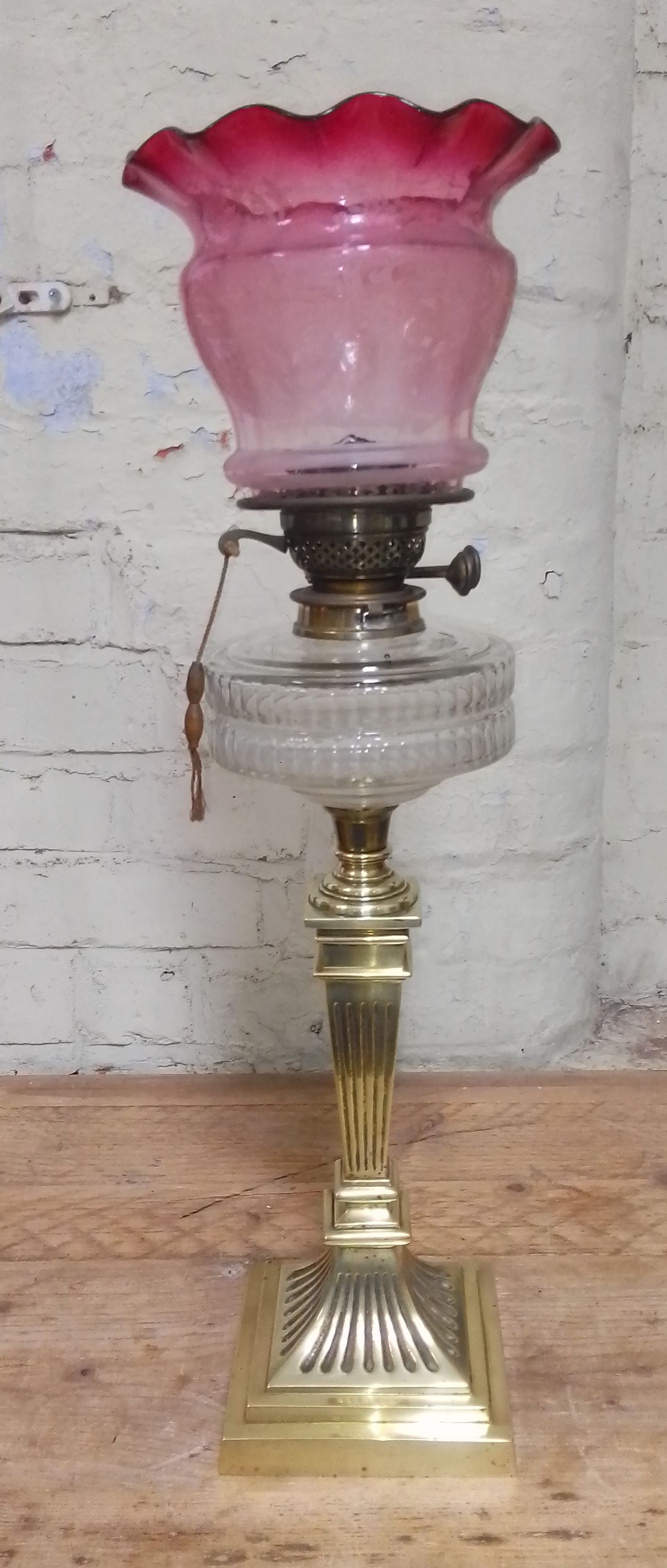 A brass column oil lamp with cut glass reservoir and cranberry glass shade.