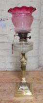 A brass column oil lamp with cut glass reservoir and cranberry glass shade.
