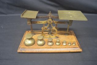 Set of Acme brass postal scales with seven weights (8oz down to 0.25oz), standing on mahogany base