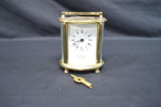 Brass and glass cased Woodford oval carriage clock with top carrying handle, white dial, Roman