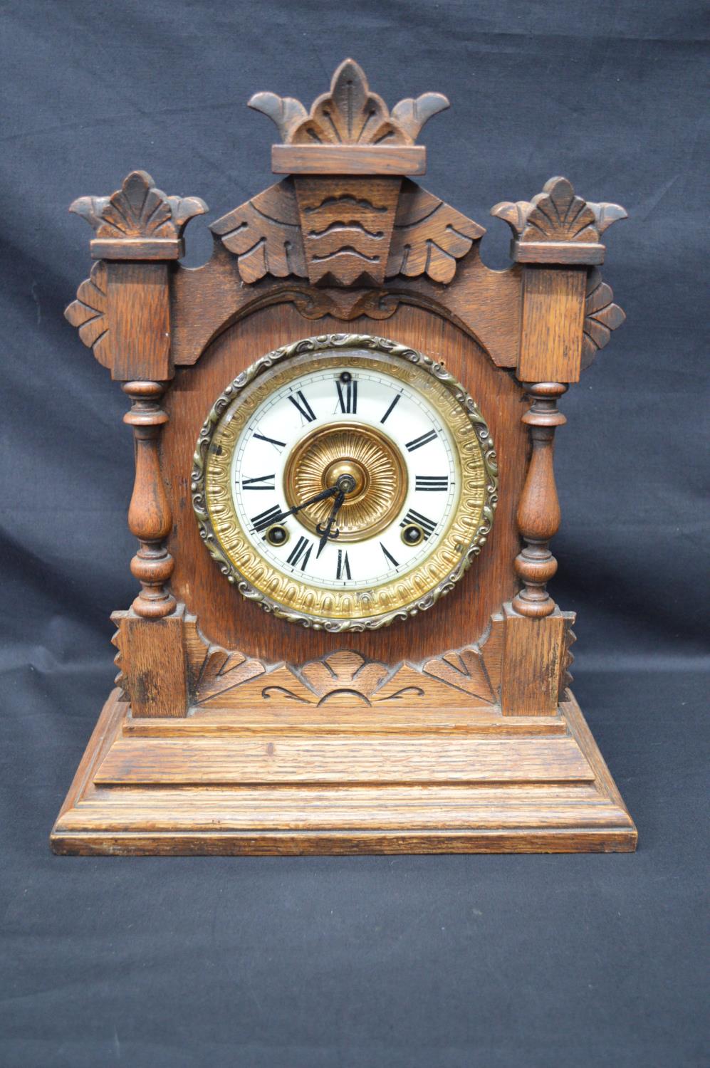 Oak cased mantle clock having some carving to case and standing on stepped base. Black hands and