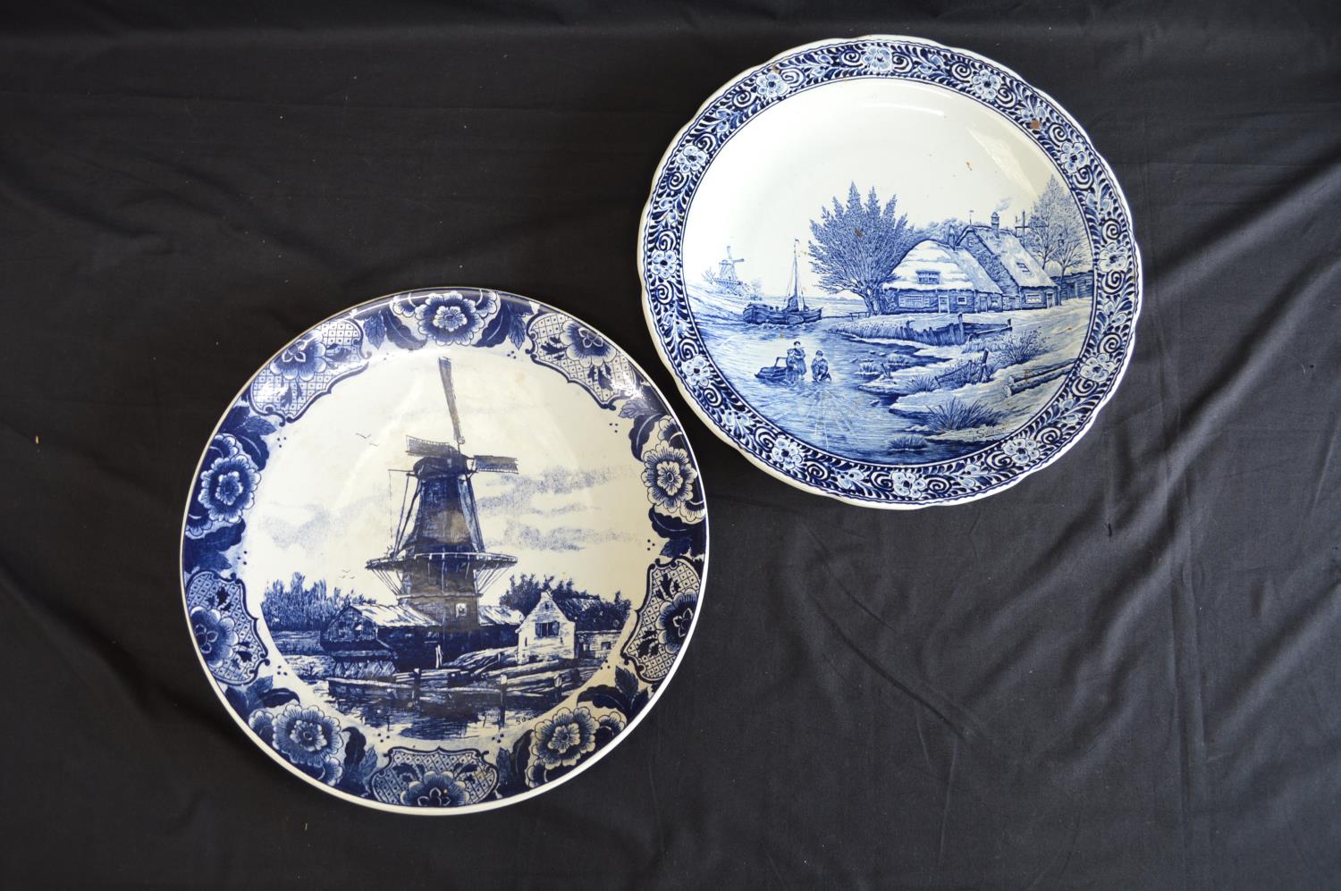 Two Delft blue and white wall hanging chargers decorated with scenes of children playing on a frozen