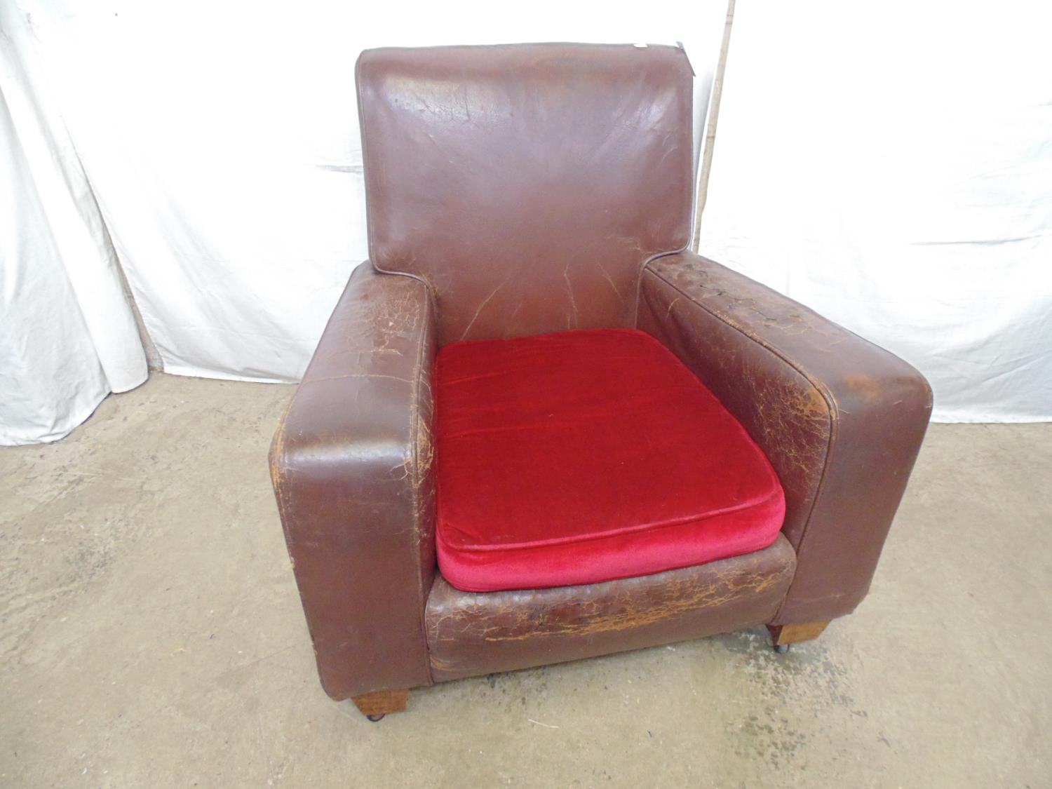 Brown leather club chair with red cushion, standing on block feet and castors (af) - 84cm x 72cm x