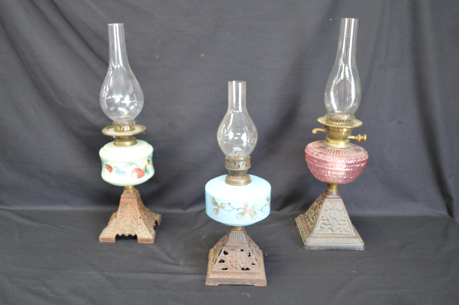 Group of three iron based oil lamps each having glass reservoir and chimney - tallest 57.5cm