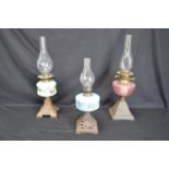 Group of three iron based oil lamps each having glass reservoir and chimney - tallest 57.5cm