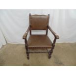 Oak elbow chair having brown leather padded back and seat with studwork detail, standing on turned