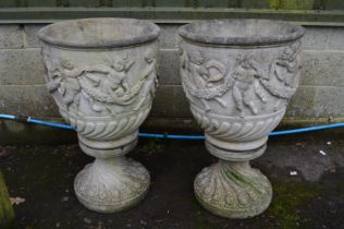 Pair of circular garden urns decorated with figures of dancing cherubs and swags, standing on